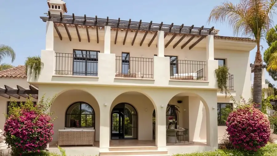 The ivory façade of La Serena: arched loggia, timber pergola and bougainvillea above the lawn